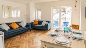 A modern living room with two sofas, a dining table set for four, and a large window with a view of the outside. - Harbour Hideaway (Looe)