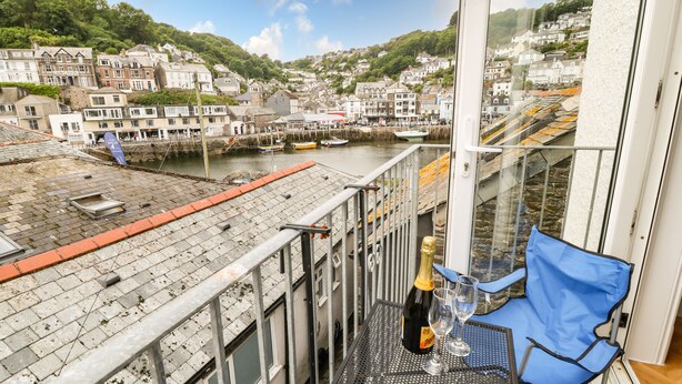 A balcony with a table, a bottle of champagne, and a glass, overlooking a harbor with boats and buildings. - Harbour Hideaway (Looe)