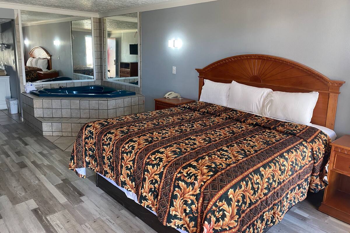 Ein Hotelzimmer mit einem großen Bett, einem hölzernen Kopfteil, einem Badezimmer mit einer Badewanne und einem großen Spiegel.
