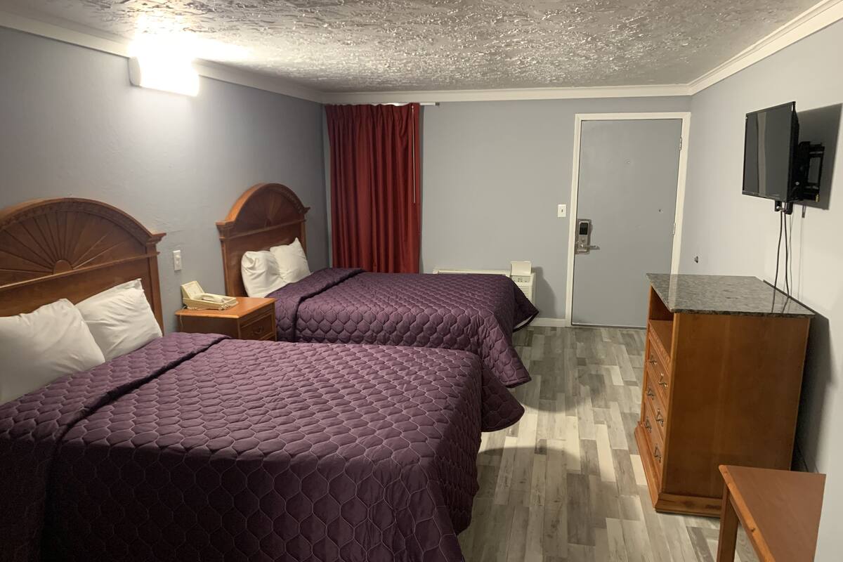 Ein Hotelzimmer mit zwei Betten, einem Holzkoffer, einem Schreibtisch, einem Fernseher und einer Tür.