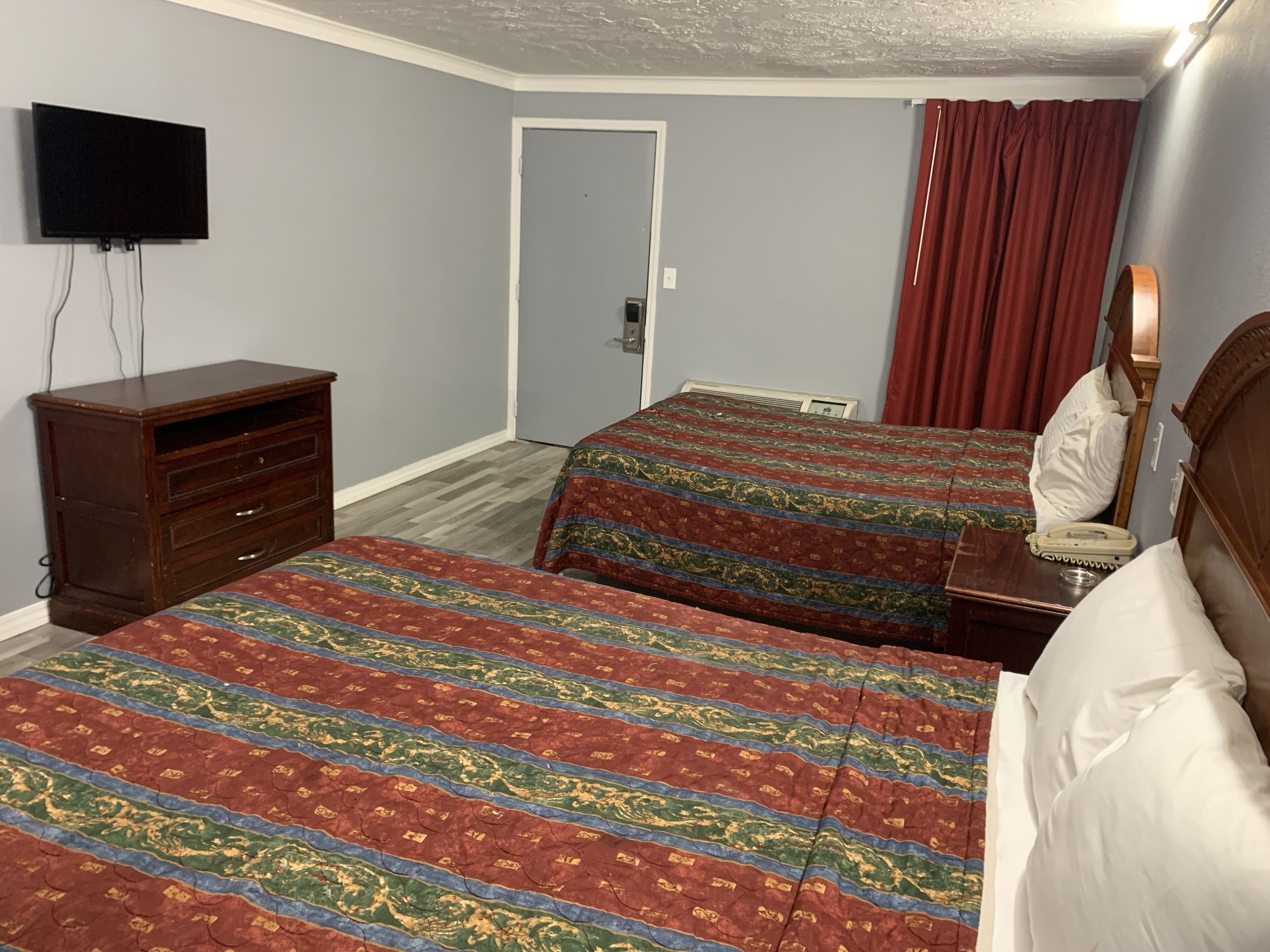 A hotel room with two beds, a dresser, a television, and a door.