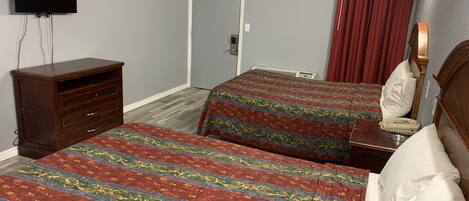 A hotel room with two beds, a dresser, a television, and a door.