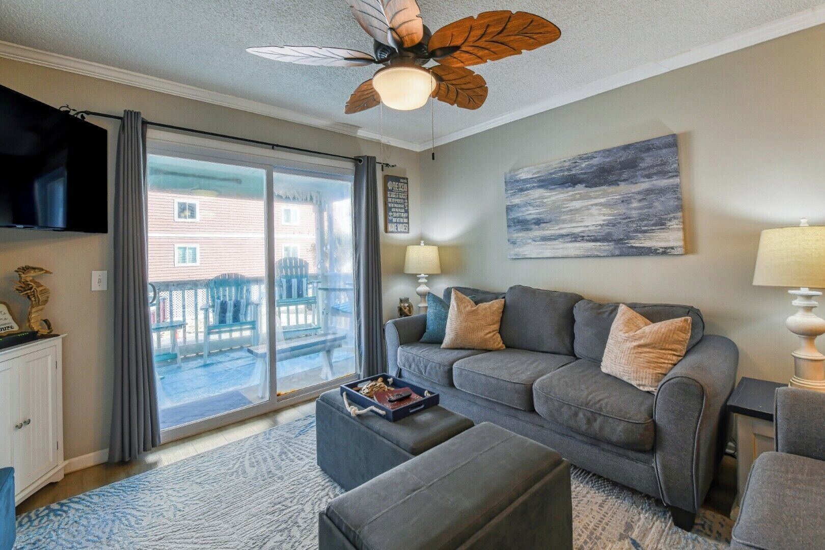 Ein Wohnzimmer mit grauem Sofa, Hocker und Deckenventilator mit Blattformdesign.