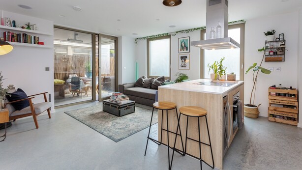 Een moderne keuken met een centraal eiland, barstoelen en een eethoek met een glazen deur naar een balkon.