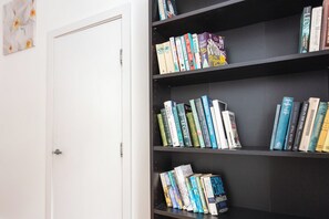 Een boekenplank met verschillende boeken, een witte deur en een muur met een bloemschilderij.