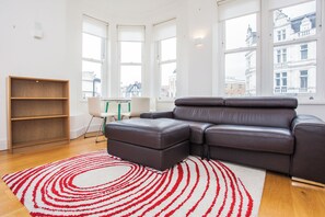 A modern living room with a leather sofa, a wooden bookshelf, and a red and white patterned rug.