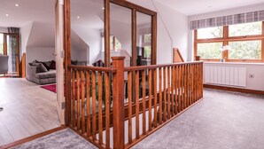 A spacious loft bedroom with a large window, a wooden staircase, and a cozy seating area. - The Barn at Mulberry Lodge (Maidstone)