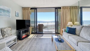 Ein Wohnzimmer mit einer Couch, einem Fernseher und einem Balkon mit Meerblick.
