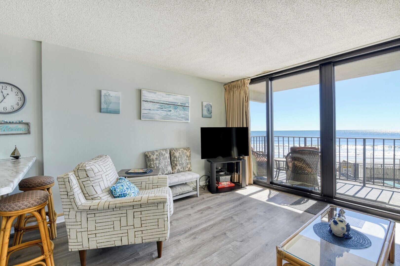Ein Balkon mit Blick auf den Strand, eine Sitzecke, ein Fernseher und ein Esstisch.