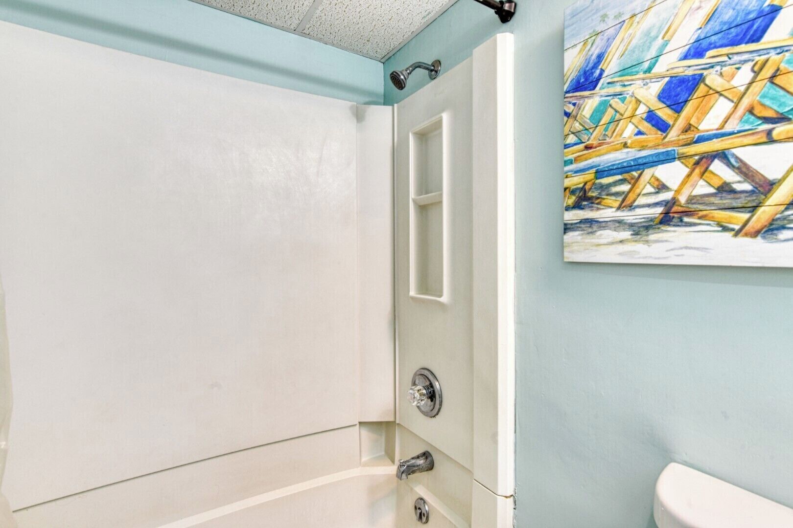 Une salle de bain équipée d’une baignoire, d’une douche et de toilettes. Un tableau représentant une scène de chantier est accroché au mur.