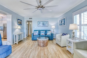 A living room with a blue sofa, white armchairs, a coffee table, and a ceiling fan.