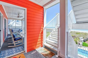 A balcony with a view of the beach, a set of white stairs, and a row of rocking chairs.