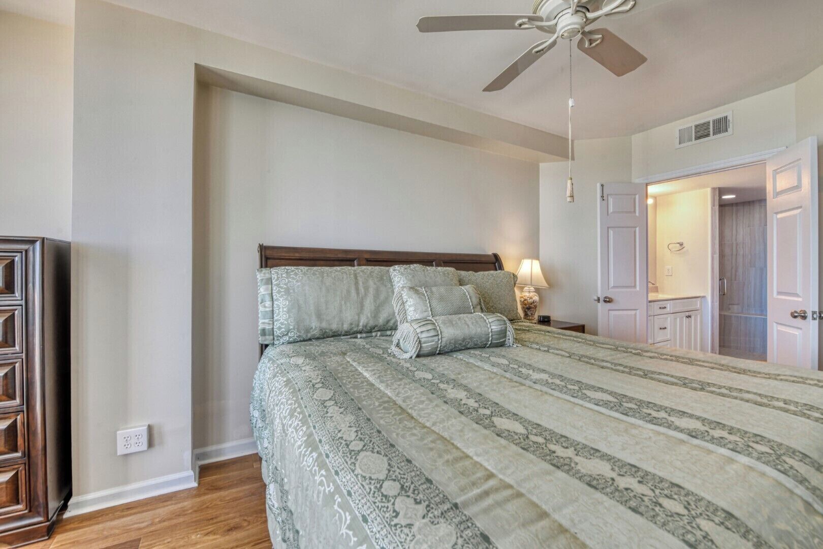 A bedroom with a bed, a ceiling fan, a nightstand, and a door leading to another room.
