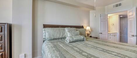 A bedroom with a bed, a ceiling fan, a nightstand, and a door leading to another room.