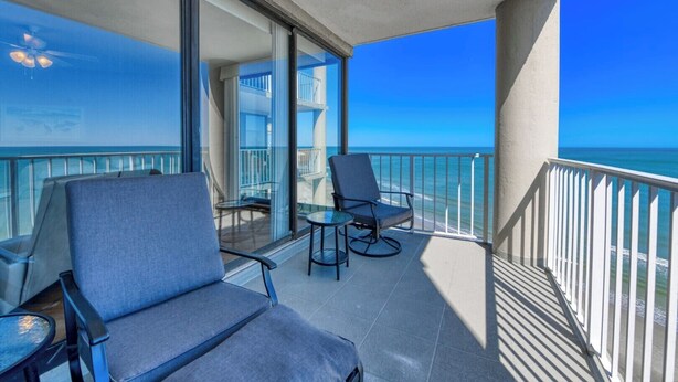 A balcony with two chairs and a small table, overlooking a clear blue sea and a building with balconies. - One Ocean Place 1207 - Fabulous 3-bedroom, 3-bath oceanfront condo (Garden City Beach)