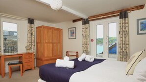 A bedroom with a bed, a desk, a chair, a wardrobe, and a view of the sea through the window.