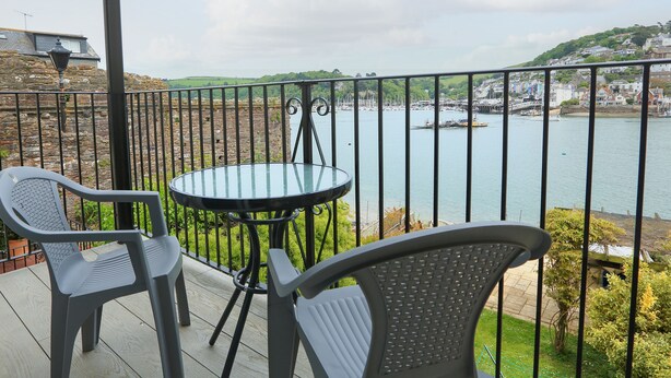 A balcony with a table and chairs overlooking a body of water and a town.