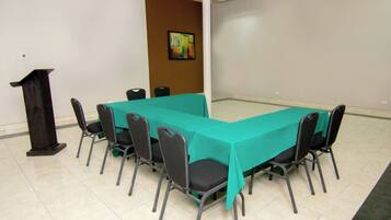 Un salón de conferencias con una larga mesa, sillas, un atril y un cuadro en la pared.