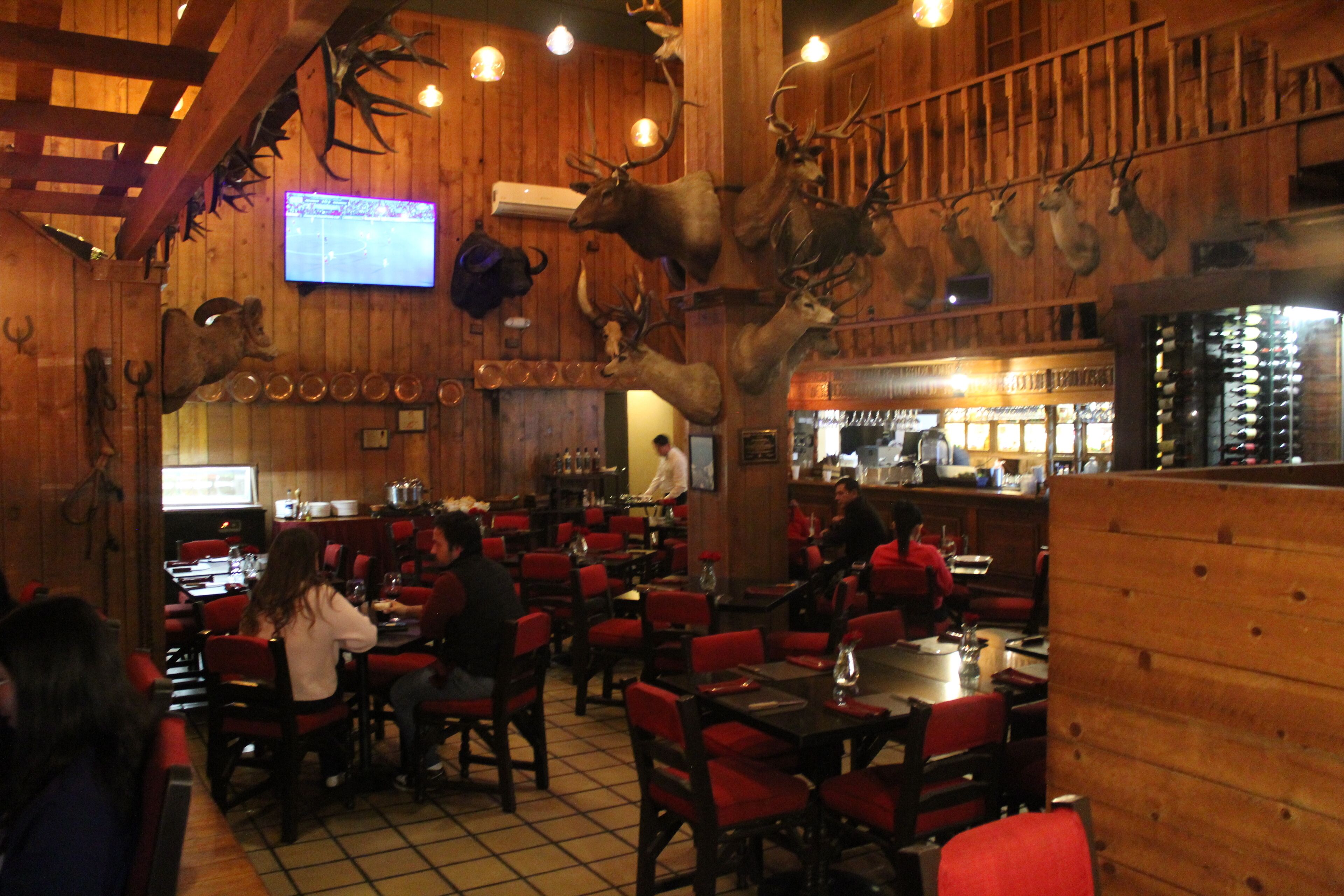 A restaurant with wooden walls, mounted animal heads, and red chairs.