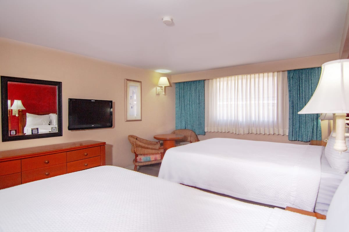 Quarto de hotel com duas camas, televisão, escrivaninha e uma cadeira.