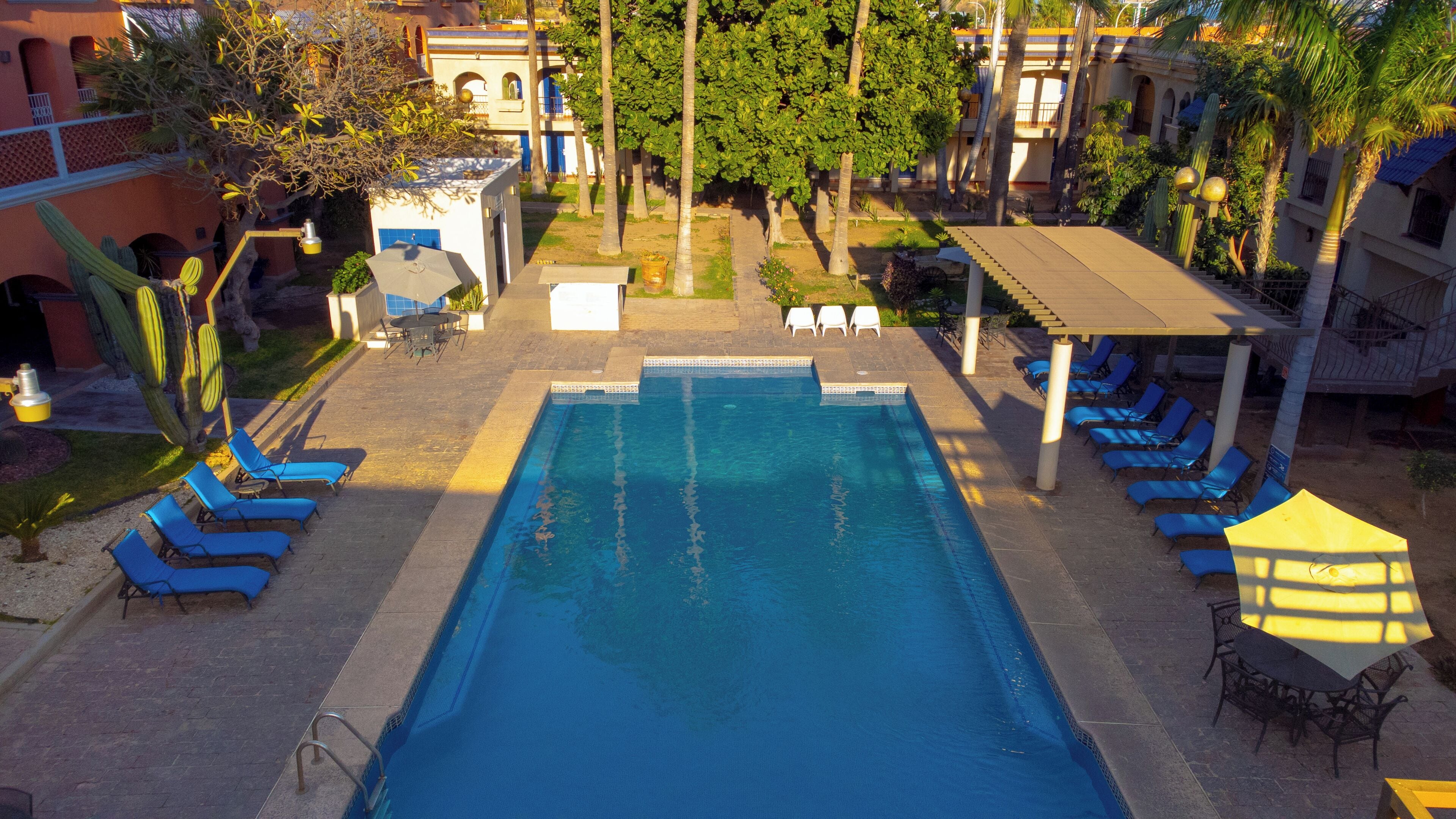 Una piscina con agua azul, rodeada de sillones de playa y sombrillas, con un edificio al fondo.