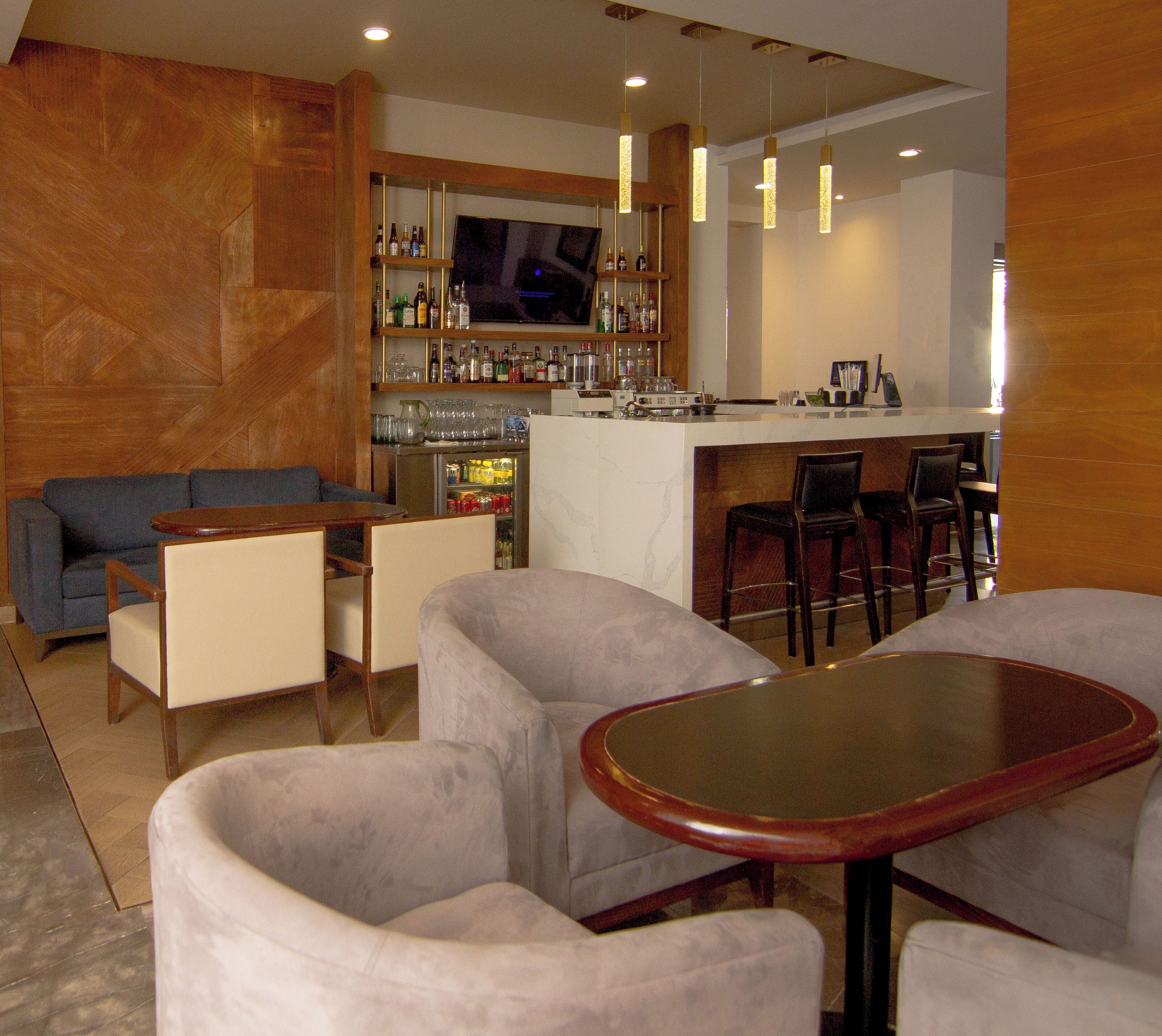 Zona de bar con televisor, taburetes y barra. Se ve un sofá y una mesa con sillas al frente.