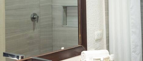 Un baño con un espejo grande, un lavamanos, una ducha y una bandeja de madera con artículos de aseo.