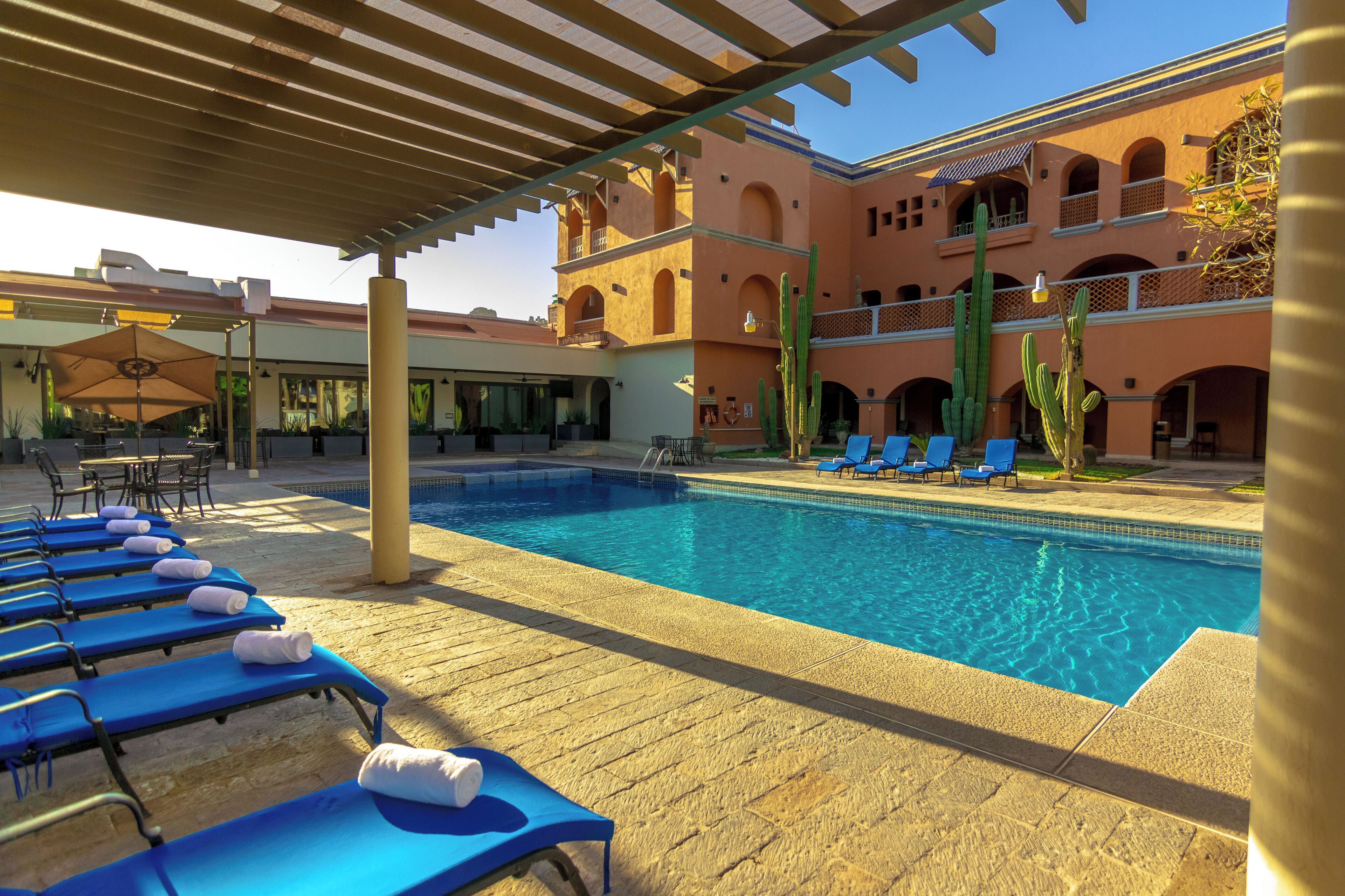 A poolside area with lounge chairs and a clear blue pool, surrounded by a building with arches and cacti.