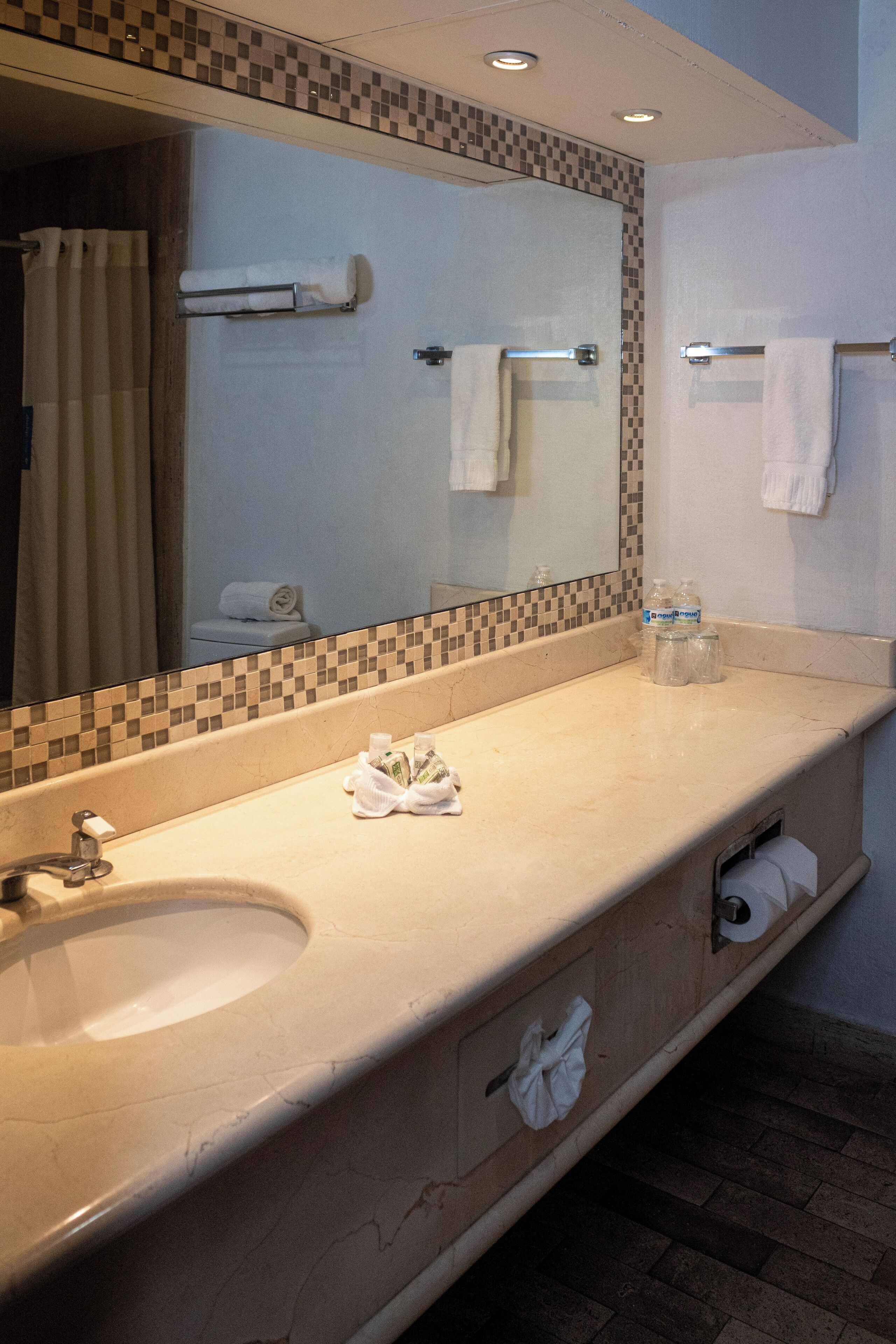 Un bagno con lavandino, specchio, porta asciugamani e schienale piastrellato.