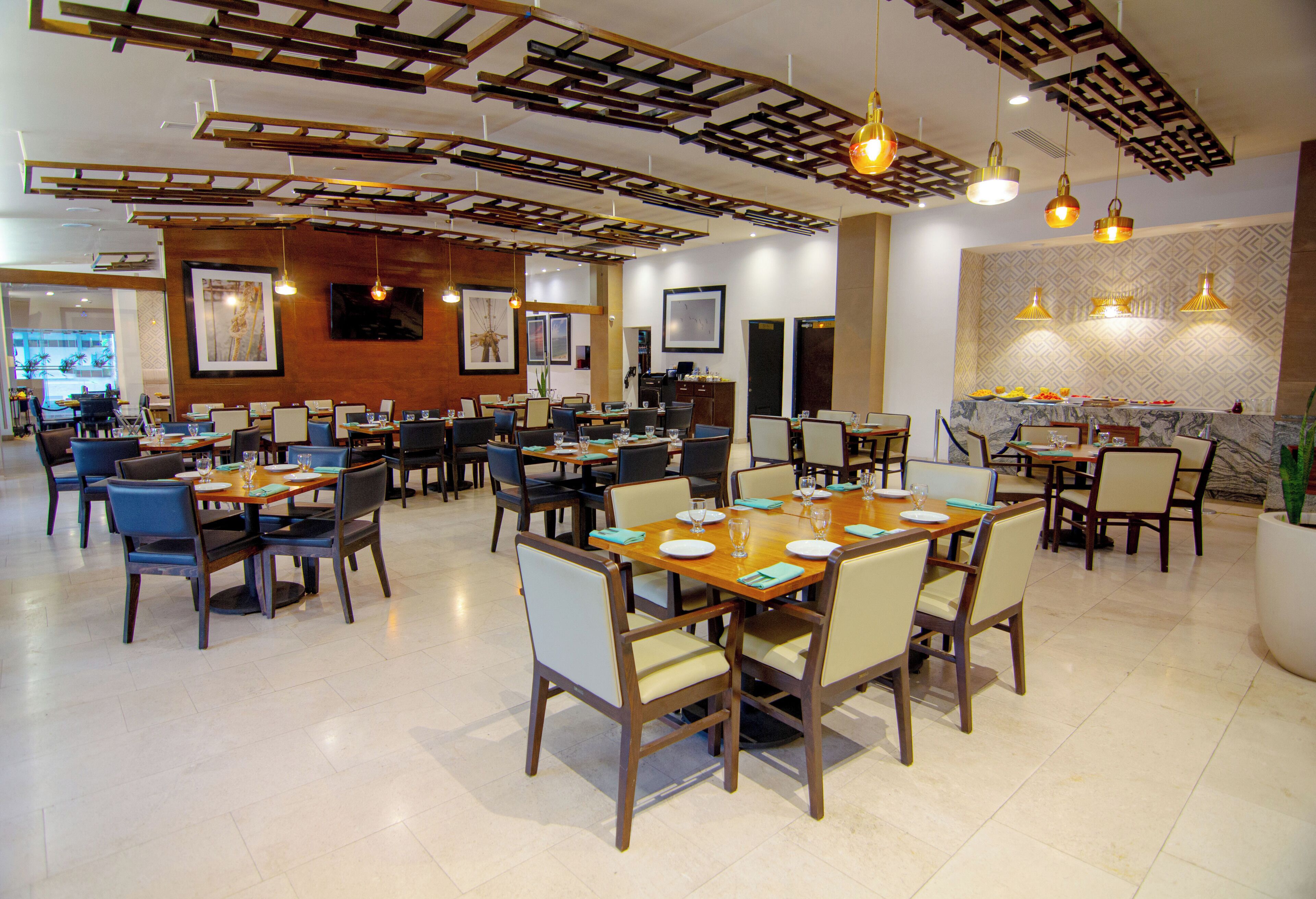 A spacious restaurant with multiple dining tables and chairs, wooden ceiling beams, and pendant lighting.