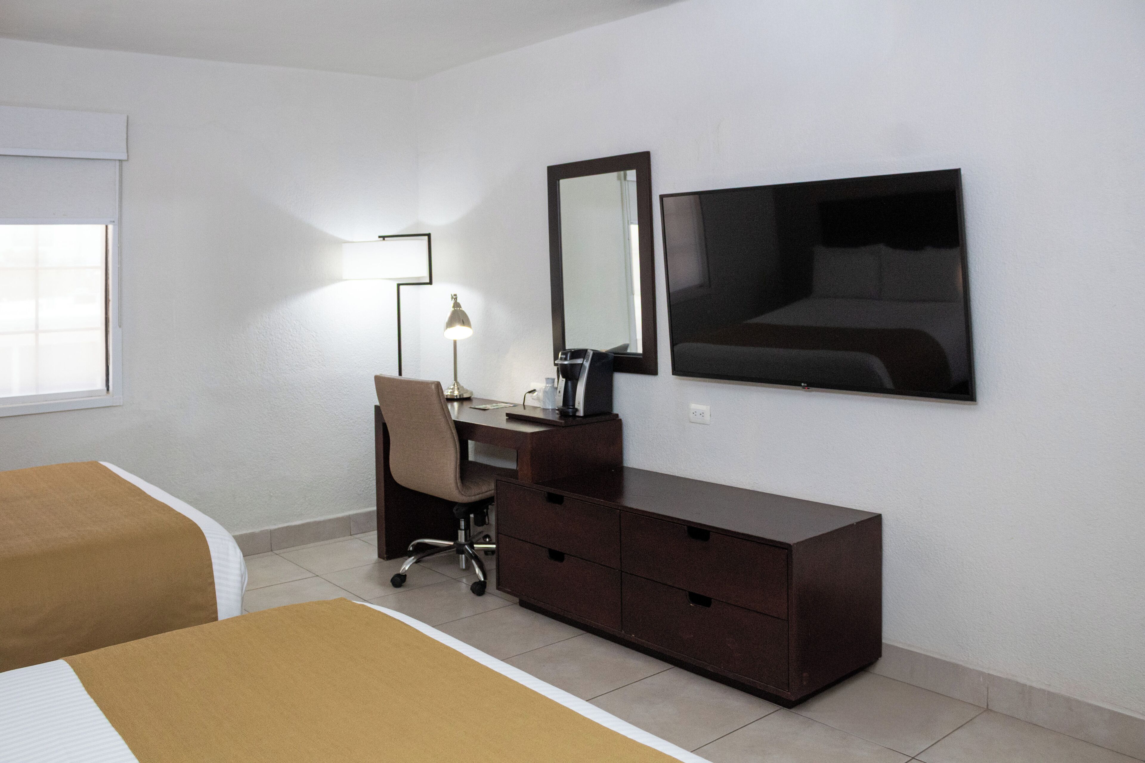 A hotel room with a bed, a desk, a chair, a dresser, a mirror, and a TV.