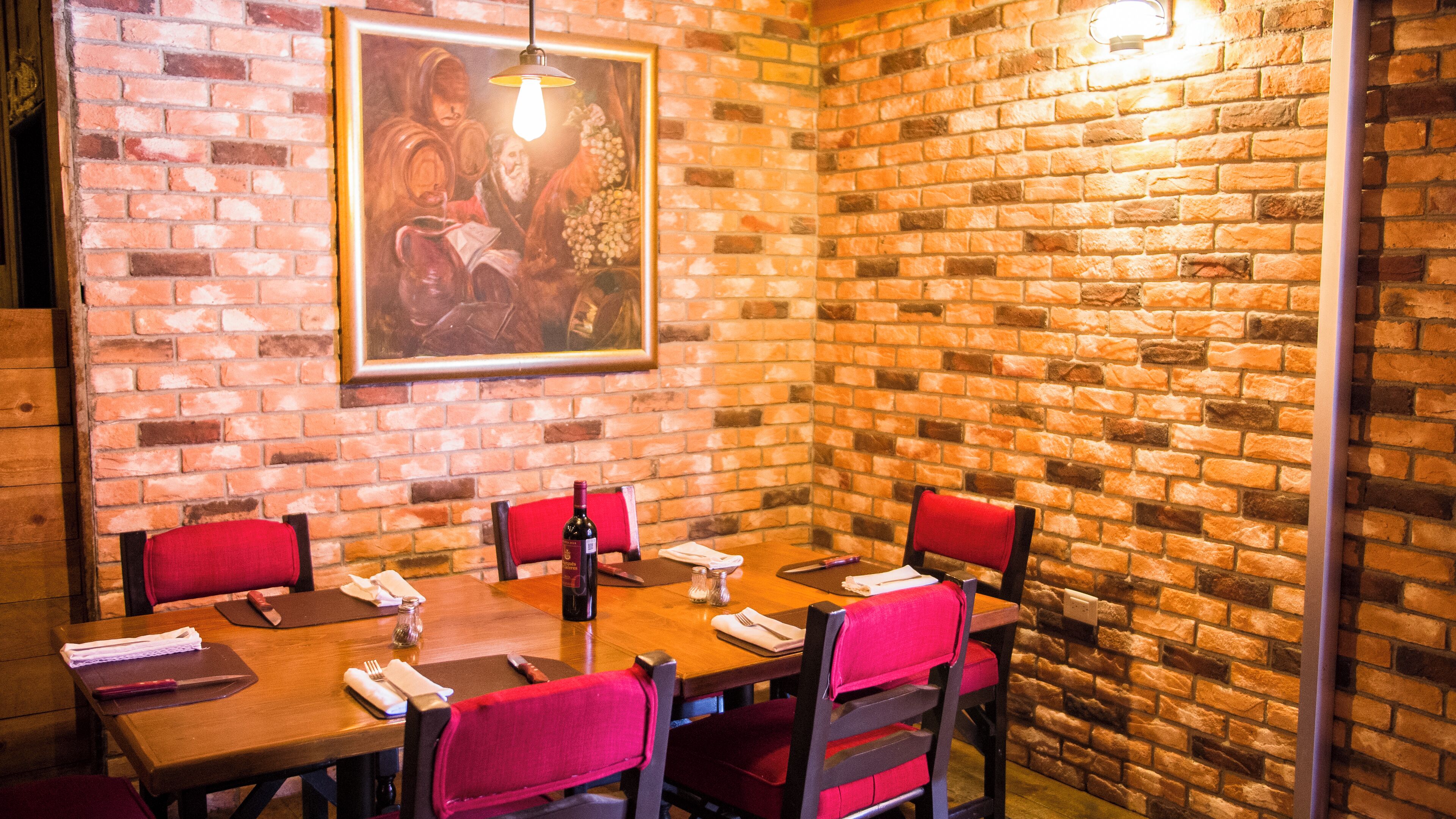 A dining area with brick walls, a wooden table, and red upholstered chairs.