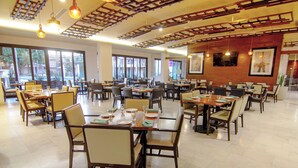 A spacious dining area with multiple tables and chairs, large windows, and a wooden ceiling design.