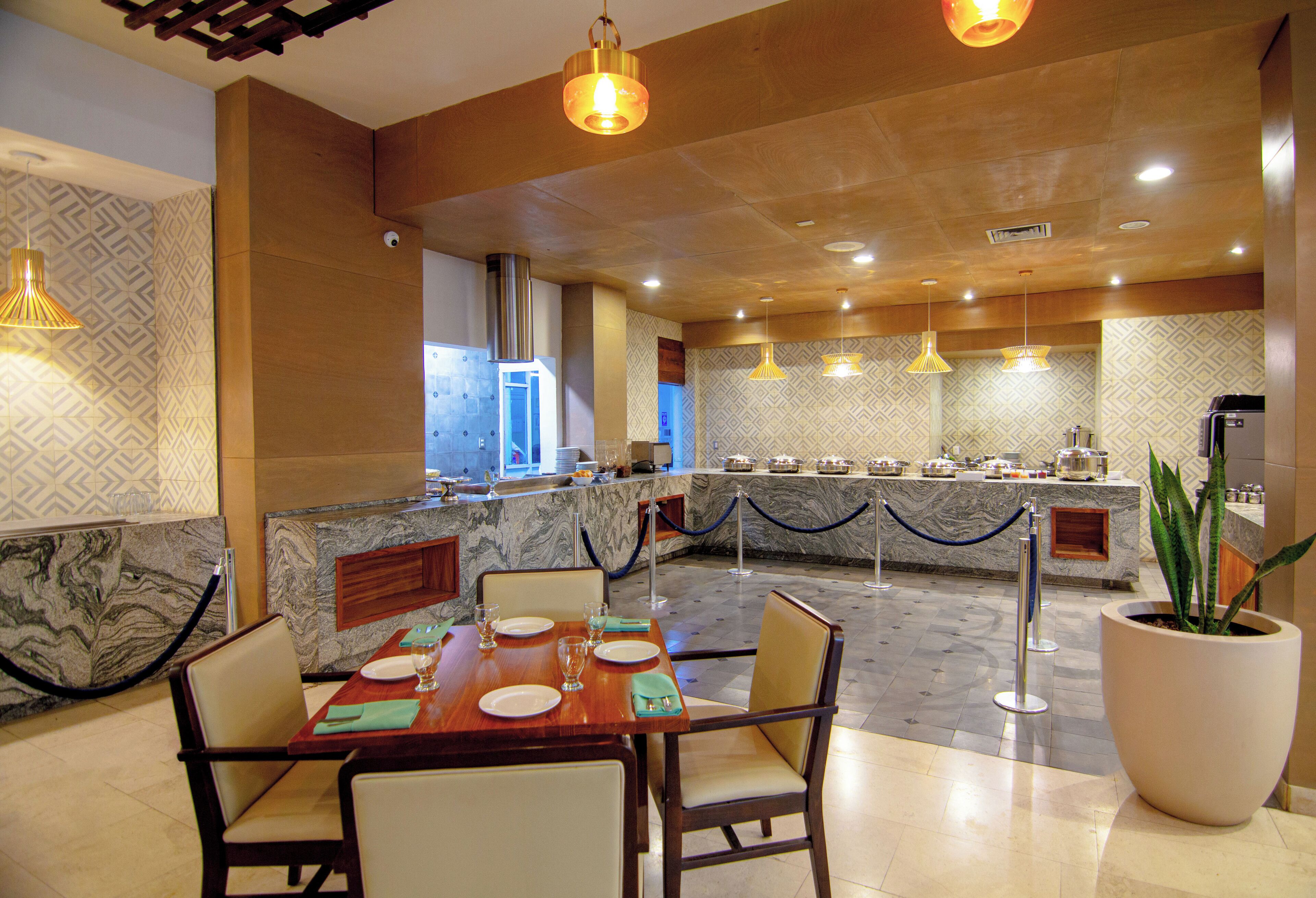 Comedor de hotel con mostradores de mármol, un bufé y una planta grande en maceta.