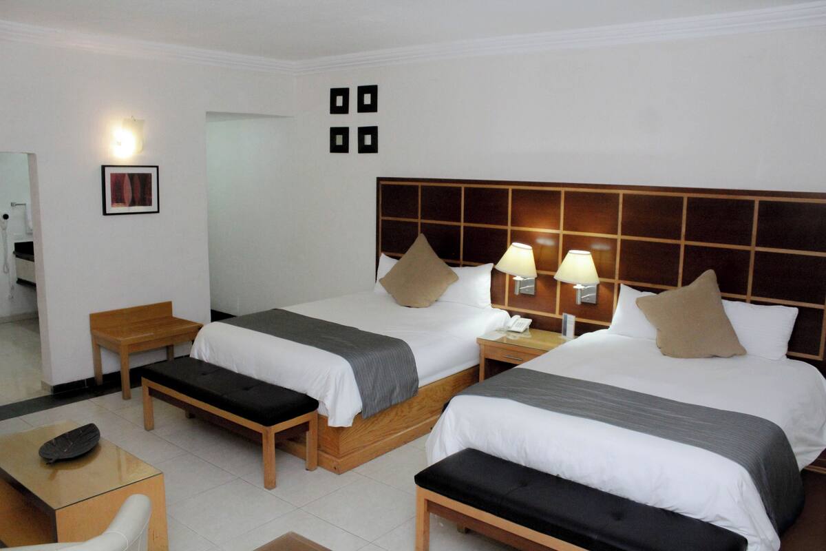 Quarto de hotel com duas camas, mesas de cabeceira, escrivaninha e uma cadeira.