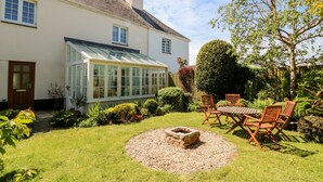 Une maison avec une véranda, un jardin doté d’un foyer extérieur et un espace salon extérieur.