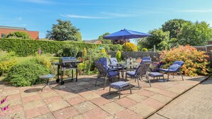 An outdoor patio with a barbecue grill, a table with chairs, and a blue umbrella. - Broadway Cottage (Lincoln)