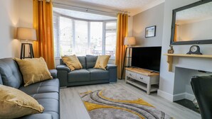 A modern living room with a grey sofa, a television, and a fireplace. - Broadway Cottage (Lincoln)