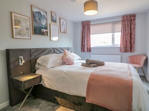 A bedroom with a bed, bedside table, and a chair. There are framed pictures on the wall and a window with curtains. - Broadway Cottage (Lincoln)