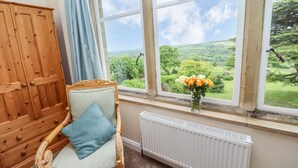 A room with a wooden wardrobe, a chair with a cushion, a radiator, and a window with a view of greenery. - Aislaby Hall (Whitby)