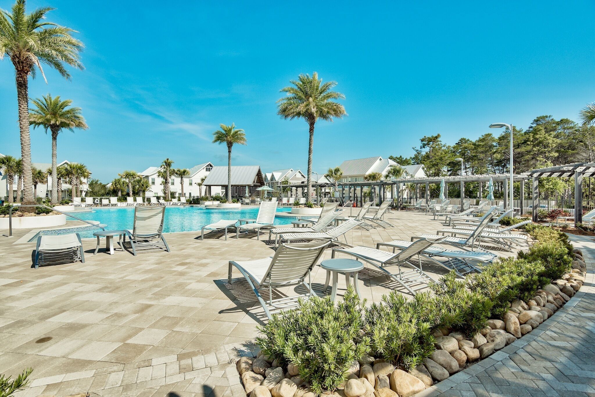 A poolside area with lounge chairs, palm trees, and a clear blue sky.