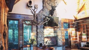 A rustic cabin interior with a stone fireplace, wooden furniture, and a mounted deer head. - Epic views! Hot tub under the stars, close to lake (Broken Bow)