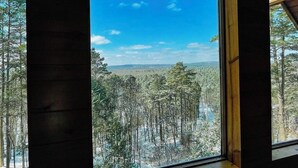 A room with a large window offering a view of a snowy forest and distant hills. - Epic views! Hot tub under the stars, close to lake (Broken Bow)