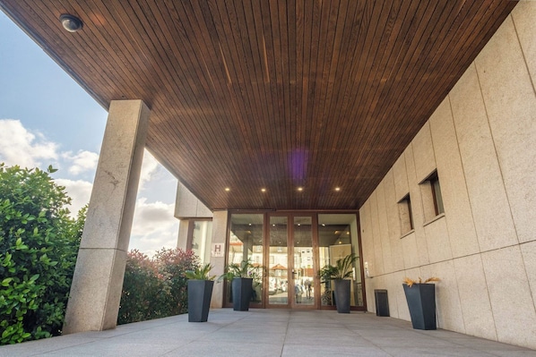 A modern building entrance with a wooden ceiling, large glass doors, and potted plants.
