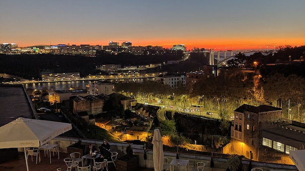 A rooftop terrace with outdoor seating, overlooking a cityscape at sunset.