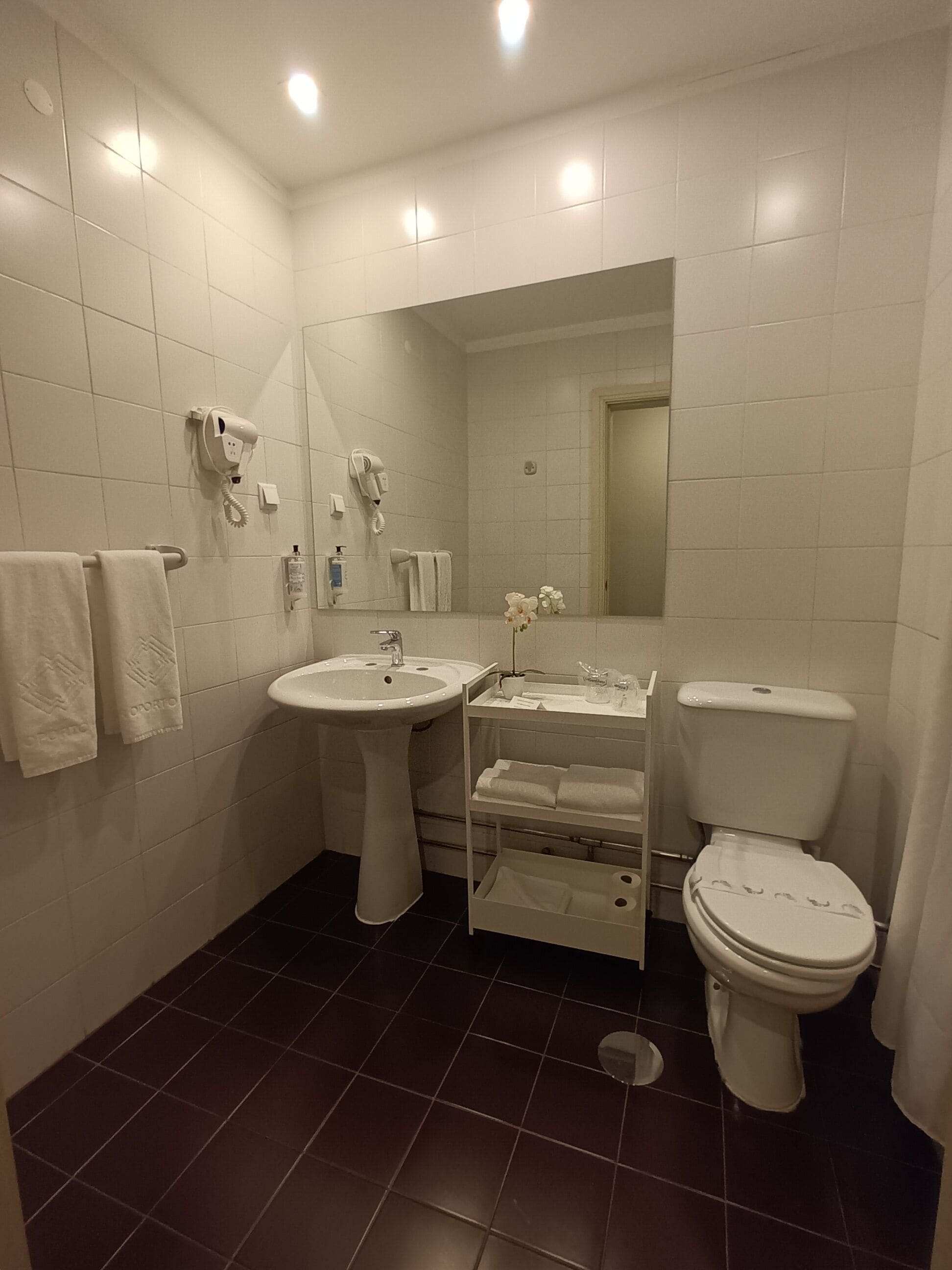 Ein modernes Badezimmer mit einem Standwaschbecken, einer Toilette und einem Waschtisch mit Spiegel. Handtücher hängen an einem Handtuchhalter und im Hintergrund ist eine Duschvorhang zu sehen.