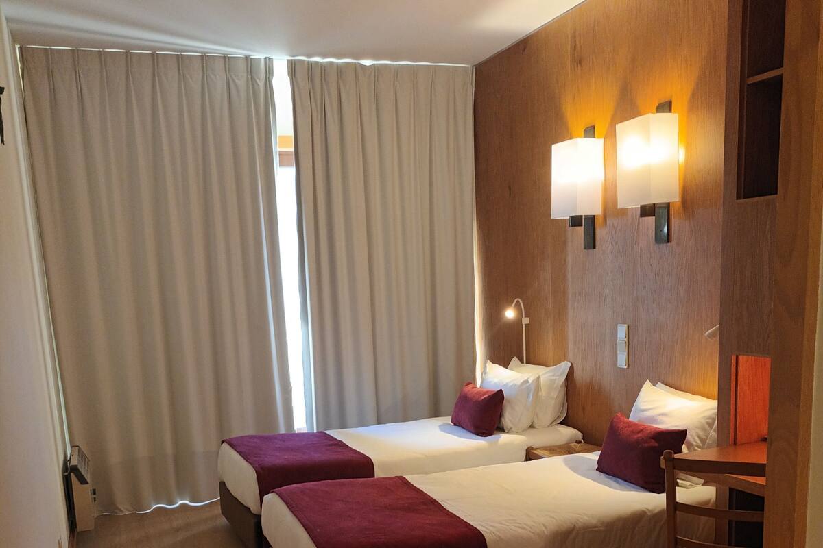 A hotel room with two beds, a wooden headboard, a desk, and a chair.