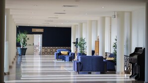 A hotel lobby with a check-in counter, seating area with sofas, potted plants, and a grand piano.