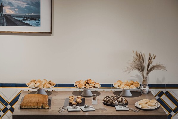 A buffet table with various pastries and desserts, a vase with dried plants, and a framed picture on the wall. - Vilar Oporto Hotel  (Porto)
