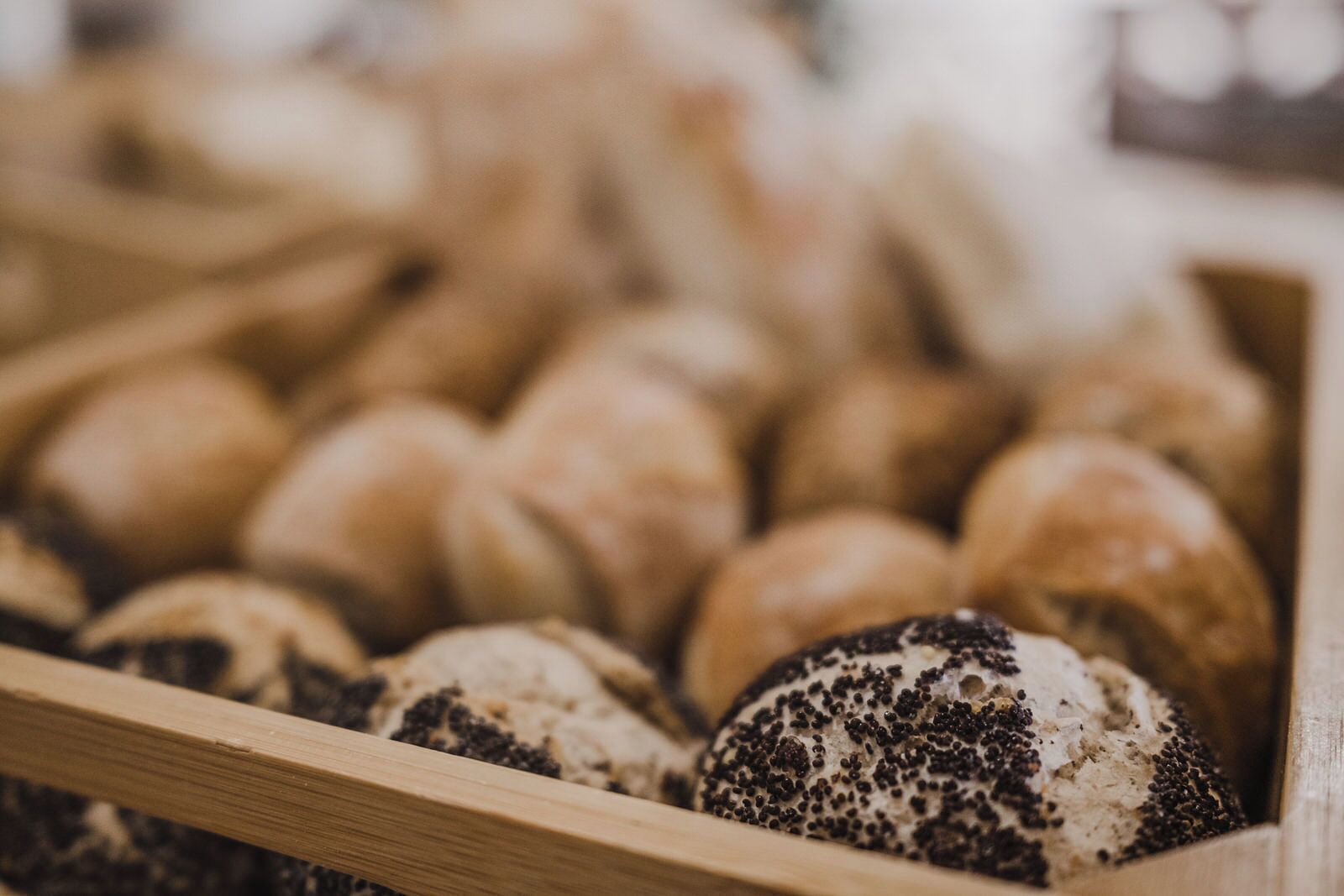 A wooden crate filled with various types of bread, including poppy seed rolls.